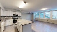 Located at 916 Main Street in downtown Buffalo, NY, this well-appointed 2-bedroom, 2-bathroom unit offers a thoughtfully designed single-level layout. The open-concept living area combines the kitchen, dining, and living spaces into one expansive, flowing room. The kitchen is a standout feature, equipped with white shaker cabinetry, a mosaic tile backsplash, granite countertops, stainless steel appliances — including a gas range, microwave, dishwasher, and refrigerator — and a central island that provides additional prep space and storage. A wall of windows along one side of the living area allows natural light to pour in, and exposed brick detailing adds an industrial character consistent with Buffalo's architectural heritage. A clean, neutral hallway connects the private areas of the unit, leading to two well-sized bedrooms, each featuring soft flooring and ample closet space — with five closets total throughout the unit. Both bathrooms are finished with marble-style tile flooring, granite-topped white vanities, and tiled shower surrounds. In-unit laundry adds everyday convenience. The consistent gray tones, white trim, and modern fixtures throughout give this unit a cohesive, contemporary feel.