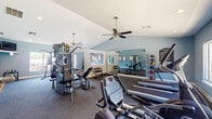 This fitness center offers a comprehensive and well-organized space designed to support a wide range of workout routines. The main exercise area features vaulted ceilings with ceiling fans that keep the space comfortable during intense workouts. The walls are painted in a calming light blue tone, complemented by white trim and durable dark rubber flooring throughout. Large wall-mounted mirrors amplify the sense of space and allow users to monitor their form while exercising.

The cardio section is equipped with multiple treadmills and a stationary bike, positioned near windows that provide natural light and views of an outdoor pool area. A multi-station strength training machine, a weight bench, and a full rack of dumbbells offer ample options for resistance and strength training. A medicine ball rack with a variety of weighted balls rounds out the functional fitness equipment.

A separate, dedicated yoga and stretching room provides a quieter, more focused environment for flexibility and low-impact workouts. This room features a large window with views of the surrounding greenery, exercise mats, a stability ball, and posted workout reference charts on the walls. A water fountain is conveniently located within the facility. Together, these spaces create a versatile, thoughtfully designed fitness environment suited for users of all fitness levels.