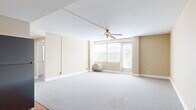This single-floor, 2-bedroom, 1-bathroom residence offers a practical and comfortable layout across a well-proportioned footprint. The combined kitchen and living room serves as the heart of the unit, with the living area featuring soft wall-to-wall carpeting, warm neutral-toned walls, a ceiling fan with light fixture, and large windows that invite natural light and provide city views. A door from the living area leads to a balcony, extending the space outdoors. The kitchen is equipped with rich dark wood cabinetry, stainless steel and black appliances including a refrigerator, range, microwave, and dishwasher, complemented by light-toned countertops and hardwood flooring. Both bedrooms are carpeted with the same neutral palette, offering a calm and quiet atmosphere. The primary bedroom is a generously sized retreat, while the second bedroom provides a comfortable secondary space, each with windows allowing natural light. The full bathroom features a tiled tub-shower combination with grab bars, a pedestal sink, and stone-style tile flooring. A hallway connects the rooms, completing this efficiently designed single-level residence.
