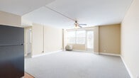 This single-floor, 2-bedroom, 1-bathroom residence offers a practical and comfortable layout across a well-proportioned footprint. The combined kitchen and living room serves as the heart of the unit, with the living area featuring soft wall-to-wall carpeting, warm neutral-toned walls, a ceiling fan with light fixture, and large windows that invite natural light and provide city views. A door from the living area leads to a balcony, extending the space outdoors. The kitchen is equipped with rich dark wood cabinetry, stainless steel and black appliances including a refrigerator, range, microwave, and dishwasher, complemented by light-toned countertops and hardwood flooring. Both bedrooms are carpeted with the same neutral palette, offering a calm and quiet atmosphere. The primary bedroom is a generously sized retreat, while the second bedroom provides a comfortable secondary space, each with windows allowing natural light. The full bathroom features a tiled tub-shower combination with grab bars, a pedestal sink, and stone-style tile flooring. A hallway connects the rooms, completing this efficiently designed single-level residence.