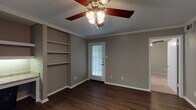 This single-story space is designed with a practical and cohesive layout that connects its key living areas seamlessly. The main living area features rich, dark hardwood-style flooring that extends throughout, complemented by neutral taupe-toned walls, crisp white baseboards, and crown molding that adds a polished architectural detail. A ceiling fan with a light fixture provides both comfort and illumination, while a door with a sidelight window allows natural light to filter in.

A standout feature of the living area is a built-in wall unit offering open shelving alongside a built-in desk with under-cabinet lighting — a functional and space-efficient element ideal for a home office setup. An open passageway connects this space to adjacent rooms, creating a natural flow throughout.

The kitchen is equipped with white cabinetry, laminate countertops, black appliances including a refrigerator, electric range, and microwave, as well as a double-basin sink. A peninsula counter provides additional workspace and delineates the kitchen from the living area.

The bedroom features plush carpeting, a large window with natural views, and a ceiling fan. The bathroom includes a single-basin vanity with laminate countertops, white cabinetry, a large mirror, and a full tub and shower combination, completing the functional layout of this well-appointed space.