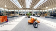Located at 1612 Sisk Rd in Modesto, California, this large-scale single-floor commercial space offers an impressive and versatile environment suited for events, gatherings, and flexible-use occupancy. The centerpiece of the space is a sweeping open atrium flooded with natural light through an expansive sawtooth skylight roof system, supported by a striking exposed beam ceiling structure that adds architectural character and visual height throughout.

The interior is organized around a wide, carpeted central floor that spans a generous open area, bordered on multiple sides by a two-story wraparound balcony with dark metal railings. The ground level features individual rooms and suites accessible through navy blue doors set against white and stone-textured walls, while the upper level mirrors this layout with balcony-facing units overlooking the main floor below.

The space is thoughtfully furnished for multi-purpose use, with modern seating clusters featuring bold orange upholstery, high-top bar tables with vibrant teal and orange chairs, and lounge areas arranged throughout. Recreational elements such as cornhole boards and a foosball table underscore the space's event-ready character. Large clerestory windows at the upper level further amplify natural light, creating a bright, welcoming atmosphere across the entire floor.