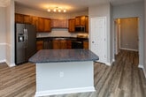 Located at 1261 Walden Legacy Way in Knoxville, Tennessee, this single-floor residence offers a thoughtfully designed open-concept layout finished with durable hardwood-style flooring throughout. The heart of the home is a well-appointed kitchen featuring rich warm-toned cabinetry, dark granite-style countertops, and a full suite of stainless steel appliances including a refrigerator with ice maker, electric range, built-in microwave, and dishwasher. A central island with a contrasting light-colored base adds additional prep and seating space, while a dedicated pantry closet provides generous storage. Track lighting illuminates the kitchen workspace effectively. The kitchen opens seamlessly into a spacious living area accented by crown molding and a ceiling fan, creating an airy and comfortable common space. Bedrooms are well-sized with large windows that invite natural light and offer views of the surrounding greenery. The bathrooms are finished consistently with the kitchen's cabinetry and countertop palette, featuring a tub-shower combination with built-in shelving. Neutral gray walls, textured ceilings, and clean white trim unify the interior with a cohesive, move-in-ready aesthetic throughout.