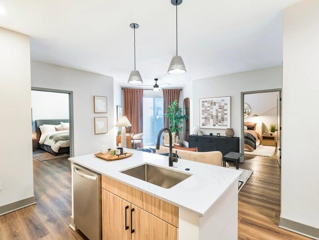 Open-concept kitchen and living area with access to dual bedrooms, warm finishes, and wood-style flooring throughout. - Modera Riverview