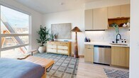 Located at 431–445 W 600 S in Salt Lake City, UT, this thoughtfully designed studio offers a contemporary living experience within a compact, single-floor layout. The open-plan living, dining, and kitchen area serves as the heart of the space, where light wood-tone flooring flows seamlessly throughout, creating a warm and cohesive aesthetic. The kitchen features flat-front cabinetry in a soft natural wood finish, a white tile backsplash, under-cabinet lighting, and stainless steel appliances, including a dishwasher — making it both functional and stylish. The living area benefits from a generously sized window that frames views of the Salt Lake City skyline and the surrounding Wasatch mountain range, filling the space with natural light. The sleeping area is well-defined and connects to two closets, offering practical storage solutions. The bathroom is finished in a modern style with light wood-tone flooring, a floating vanity with warm wood cabinetry, a white countertop, black hardware accents, and an arched mirror. White walls throughout the unit provide a clean, bright backdrop that enhances the sense of openness. Recessed lighting adds to the contemporary feel, while the overall design balances minimalism with functional comfort.