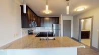 This single-floor residence combines contemporary design with functional living spaces. The kitchen serves as a central highlight, equipped with rich dark-stained cabinetry that extends to the ceiling, providing ample storage. A large granite-topped island with an undermount sink and pendant lighting anchors the space, complemented by a subway tile backsplash and a full suite of stainless steel appliances, including a refrigerator, range, and built-in microwave. Wood-look flooring runs throughout the kitchen and adjoining areas.

The bedrooms are distinguished by striking arched windows that frame outdoor views of a nearby waterway and surrounding landscape, flooding the rooms with natural light. One bedroom features soft carpeting, while another showcases wood-look plank flooring, each offering a comfortable, well-proportioned space.

Two bathrooms mirror each other in design, each featuring dark vanity cabinetry with granite countertops, an undermount sink, and a tub-shower combination. Light-toned tile flooring and recessed lighting contribute to a clean, modern aesthetic throughout both bathrooms. The overall unit presents a cohesive, contemporary palette of neutral tones and dark wood accents.