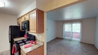 This single-floor residence offers a functional and comfortable layout across its living spaces. The kitchen is designed in a galley style, featuring warm medium-toned wood cabinetry, granite-look laminate countertops, and black appliances including a refrigerator, electric range, and over-the-range microwave. A single-basin sink and tile-style flooring complete the kitchen's practical setup. The kitchen opens directly into the living area, creating a connected feel between the two spaces.

The living room is carpeted and bathed in natural light from a large sliding glass door fitted with vertical blinds, which leads to an outdoor balcony. The open layout provides a versatile space suitable for various furniture arrangements.

The bedroom is generously sized, featuring plush carpeting, a ceiling fan with a light fixture, and notable storage provided by a double bifold closet with full-length hanging rods — offering ample organizational capacity.

The bathroom is accessed via a hallway and includes a wood-toned vanity with an undermount sink, a lighted mirror, tile-look flooring with a striped area rug, and a textured ceiling. The overall ambiance of the space is neutral and move-in ready.