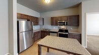 Located at 218 19th St SE in Watertown, South Dakota, this single-floor unit offers a well-organized and functional layout throughout. The kitchen is a standout feature, outfitted with rich dark-stained cabinetry, granite countertops, and a full suite of stainless steel appliances including a refrigerator, electric range, over-the-range microwave, and dishwasher. A granite-topped island provides additional prep and dining space, while light wood-look flooring ties the kitchen and adjoining living area together seamlessly. The open layout connects the kitchen to the living space, which benefits from natural light through a large sliding door with vertical blinds. The bedrooms are carpeted for comfort and each feature windows with blinds and baseboard heating. The primary bathroom includes a vanity with granite countertops and convenient access to a walk-in closet. A second full bathroom features a tub-shower combination and matching granite vanity. A dedicated laundry area houses a full-size washer and dryer and includes wire shelving for additional storage. Textured ceilings are present throughout, adding character to the neutral, move-in-ready interior. The overall ambiance is clean, practical, and well-appointed for everyday living.