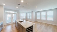 This well-appointed single-story home in Humble, Texas offers a thoughtfully designed open-concept layout that seamlessly connects the kitchen, dining, and living areas. The kitchen serves as the centerpiece of the home, showcasing a large island with a striking quartz countertop, an undermount sink, and a built-in wine rack. Two-tone cabinetry — white uppers paired with gray lowers — frames stainless steel appliances, including a refrigerator, microwave, and range, all set against a classic subway tile backsplash. Light hardwood flooring flows throughout the main living areas, complementing the neutral color palette and recessed lighting overhead. Multiple windows fitted with white horizontal blinds fill the open living space with abundant natural light. French doors provide additional brightness and exterior access. The primary bathroom features a glass-enclosed walk-in shower with tile surround, dual-sink vanity with quartz countertops, and gray cabinetry. The secondary bathroom offers a tiled tub-shower combination and a single vanity. A well-lit hallway connects the two bedrooms, both of which are carpeted for comfort. The home's clean, contemporary finishes and efficient floor plan make it a practical and attractive residence.