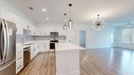 Located at 125 Town Center Dr in Garden City, GA, this single-story 2-bedroom, 2-bathroom home offers a thoughtfully designed open-concept layout with clean, modern finishes. Light hardwood-style flooring flows consistently throughout the entire space, complementing the bright white walls and creating a cohesive, airy feel.

The kitchen is a standout feature, showcasing white shaker cabinetry, a subway tile backsplash, white quartz countertops, and a full suite of stainless steel appliances including a refrigerator, range, microwave, and dishwasher. A large center island provides additional prep space and seating, while stylish pendant lights and a sputnik chandelier add contemporary character to the open dining area beyond.

Both bedrooms are well-proportioned and filled with natural light from windows with horizontal blinds. The primary bedroom includes its own dedicated closet space with built-in wire shelving systems offering generous storage. A second closet serves additional organizational needs.

Each bathroom features white shaker vanity cabinetry, white quartz countertops, undermount sinks, matte black hardware, large framed mirrors, and tiled shower enclosures. The design is consistent and polished throughout.

The living area benefits from abundant natural light through large windows, with views of the surrounding greenery, creating a welcoming and comfortable atmosphere throughout this well-appointed home.
