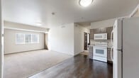 Located at 1928 N Main St in Aberdeen, South Dakota, this well-appointed unit offers four bedrooms and three bathrooms across a single, thoughtfully designed floor. The open-concept living and kitchen area serves as the heart of the space, featuring dark hardwood-style flooring that transitions into plush carpet in the living zone. The kitchen is fully equipped with a range, over-the-range microwave, and refrigerator, complemented by taupe cabinetry and light countertops. A built-in entryway organizer with cubbies and hooks provides convenient storage near the main entrance. Each bedroom is carpeted and features neutral walls, natural light from windows with blinds, and ample room for furnishings. The bedrooms are well-suited for individual use, with some featuring tray ceilings that add architectural interest. The bathrooms are cleanly finished — one highlights a wide vanity with dark cabinetry, a large mirror, and tile flooring, while others include full tub-shower combinations with wood-toned doors. The overall aesthetic is clean, modern, and functional, with a neutral palette of whites, grays, and warm wood tones throughout, creating a cohesive and comfortable living environment.