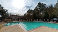 Located at 3414 Shortcut Rd in Pascagoula, Mississippi, this single-story property offers a welcoming outdoor amenity area centered around a spacious swimming pool. The pool features clear turquoise water and is finished with a tiled surround, with depth markers visible along the edges. A broad concrete deck encircles the pool, lined with numerous lounge chairs that provide ample space for relaxation and recreation. The pool area is enclosed by a wrought iron fence, ensuring both security and an open, airy feel. Towering pine trees form a natural backdrop along the perimeter, offering shade and a sense of privacy while contributing to the serene, nature-surrounded atmosphere. The overall setting benefits from abundant natural light, with an open sky overhead that enhances the outdoor experience. The lush tree line and well-maintained pool deck create an inviting environment suitable for leisure and outdoor gatherings. This property's outdoor space reflects a practical yet comfortable design, making it a notable feature of the Pascagoula community setting.