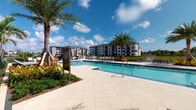 Located at 400 SW 27th Ave in Fort Lauderdale, Florida, this resort-style pool area delivers a refined outdoor living experience designed for relaxation and leisure. At its centerpiece is a generously sized swimming pool with crystal-clear blue water, framed by a wide, light-toned tile deck that provides ample space for sunbathing loungers and poolside seating. Lush tropical landscaping — including tall swaying palms, vibrant bromeliads, and manicured greenery — creates a vivid, resort-like ambiance throughout the space.

A beautifully designed covered pavilion anchors the pool area, featuring vaulted ceilings accented with exposed wood beam trusses and crisp white shiplap-style walls. Large glass panel doors and windows flood the interior with natural light while maintaining open sightlines to the pool and surrounding landscape. The pavilion's covered terrace is furnished with plush outdoor sofas and stylish lattice-patterned lounge chairs, offering a comfortable shaded retreat.

Wide tiled walkways connect the various zones of the outdoor space, ensuring easy circulation between the pool deck, pavilion, and landscaped garden areas. The combination of modern architectural detailing, tropical flora, and thoughtfully curated outdoor furnishings creates an inviting, upscale atmosphere ideal for both relaxation and social gatherings in the South Florida sun.