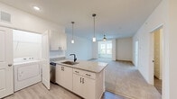 Located in Fuquay-Varina, NC, this single-floor, 3-bedroom, 3-bathroom home offers a clean, modern design with a bright and open layout. The kitchen is a standout feature, boasting white shaker cabinetry with matte black hardware, granite countertops, a center island with an undermount sink, and stainless steel appliances including a refrigerator, range with wall-mounted hood, and dishwasher. Pendant lighting over the island and recessed ceiling lights enhance the space, which flows seamlessly into the open living area. The living room is fitted with plush carpet, a ceiling fan, and a window that invites natural light. The generously sized primary bedroom features soft carpet flooring, a ceiling fan, and direct access to a walk-in closet equipped with wire shelving. A built-in granite-topped shelf adds a functional touch to one of the secondary rooms, which also feature neutral carpet throughout. The bathrooms are finished with clean white tile surrounds and matte black fixtures. In-unit laundry is conveniently located within the kitchen area. The home's consistent use of light tones, modern finishes, and efficient layout creates a fresh and functional living environment.