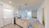 Located in Fuquay-Varina, NC, this single-floor, 3-bedroom, 3-bathroom home offers a clean, modern design with a bright and open layout. The kitchen is a standout feature, boasting white shaker cabinetry with matte black hardware, granite countertops, a center island with an undermount sink, and stainless steel appliances including a refrigerator, range with wall-mounted hood, and dishwasher. Pendant lighting over the island and recessed ceiling lights enhance the space, which flows seamlessly into the open living area. The living room is fitted with plush carpet, a ceiling fan, and a window that invites natural light. The generously sized primary bedroom features soft carpet flooring, a ceiling fan, and direct access to a walk-in closet equipped with wire shelving. A built-in granite-topped shelf adds a functional touch to one of the secondary rooms, which also feature neutral carpet throughout. The bathrooms are finished with clean white tile surrounds and matte black fixtures. In-unit laundry is conveniently located within the kitchen area. The home's consistent use of light tones, modern finishes, and efficient layout creates a fresh and functional living environment.