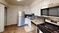 Located in Columbia, Maryland, Unit 202 at 5764 Stevens Forest Rd is a thoughtfully designed single-floor residence that balances comfort and functionality. The living area is generously sized, featuring plush wall-to-wall carpeting, neutral cream-toned walls, and abundant natural light streaming through large windows dressed with vertical blinds. A ceiling fan with integrated lighting adds both practicality and a finishing touch to the space. Sliding glass doors connect the living area to an outdoor area, offering pleasant views of the surrounding greenery.

The kitchen has been updated with crisp white shaker-style cabinetry, granite countertops, and a classic blue subway tile backsplash. Stainless steel appliances — including a refrigerator, gas range, microwave, and dishwasher — complete this functional and stylish cooking space. Wood-look flooring ties the kitchen together with a clean, modern aesthetic.

The bedrooms continue the carpeted, light-filled theme, each offering ample space and natural light through large windows. The unit includes two full bathrooms: one featuring a soaking tub with a shower and a white vanity, and a second with a standalone glass-enclosed shower stall. Both bathrooms feature wood-look flooring and clean, neutral finishes throughout.