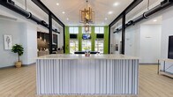 This contemporary single-floor community clubhouse offers a well-appointed, open layout designed for both social interaction and practical use. The space is defined by soaring double-height ceilings, bold black structural columns, and exposed ductwork that lend an industrial-chic character throughout.

The reception area serves as the focal point upon entry, featuring a sleek, ribbed-panel front desk topped with a marble-style surface, illuminated by a striking geometric gold chandelier. Vibrant lime-green accent walls and large windows frame views of the outdoors, flooding the space with natural light. Multiple wall-mounted TVs are positioned throughout for convenience and entertainment.

Adjacent to the reception, a dedicated workstation area offers a built-in counter with seating, a wall-mounted display, and a quiet nook for focused tasks.

The kitchen area is fully equipped with stainless steel appliances — including a range, refrigerator, and range hood — complemented by gray cabinetry, marble-look countertops, and a dramatic dark geometric tile backsplash. Pendant lighting adds a refined touch.

The lounge area is generously sized, featuring a pool table, comfortable seating arrangements, and direct access to the outdoors through large glass doors, making it an ideal gathering space for residents.