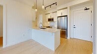 Located at 20142 53A Avenue in Langley, BC, this well-appointed two-bedroom, one-bathroom unit offers a thoughtfully designed layout with modern finishes throughout. The open-concept kitchen is a standout feature, equipped with white shaker-style cabinetry, stainless steel appliances including a refrigerator, stove, and built-in microwave, and a sleek light-toned countertop peninsula with an undermount sink. Pendant lighting and track lighting illuminate the space, complementing the light hardwood-style flooring that flows through the main living areas. The generously sized primary bedroom provides ample space and is finished with plush carpeting and crisp white walls, creating a calm and comfortable retreat. The second bedroom, also carpeted, offers a bright and versatile space suitable for a variety of uses. The full bathroom features a combined tub and shower, a vanity with wood-toned cabinetry, light quartz countertops, a large mirror, and tile flooring — all finished in a clean, contemporary style. A dedicated laundry area houses a stacked front-load washer and dryer unit for added convenience. A closet provides practical storage, rounding out this efficiently planned home with a fresh, modern aesthetic.