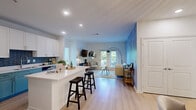 Located at 1502 Benton Blvd in Savannah, GA, this well-appointed 2-bedroom, 1-bathroom home offers a thoughtfully designed open-concept layout across a single floor. Light wood flooring flows throughout, tying together the living, dining, and kitchen areas seamlessly. The kitchen is a standout feature, boasting two-tone cabinetry — white uppers paired with soft teal lowers — complemented by a blue-gray subway tile backsplash, stainless steel appliances, and a spacious white quartz island with bar seating. The adjacent dining area is distinguished by subtly striped walls, a statement beaded chandelier, and paired arched gold-framed mirrors. The living room is anchored by a striking botanical-print accent wall and floor-to-ceiling glass doors that invite abundant natural light and outdoor views. The primary bedroom is generously sized with a bright window and light, neutral tones. The second bedroom mirrors this calm aesthetic. The shared bathroom features a double-sink vanity with teal cabinetry, chrome fixtures, a large mirror with globe lighting, and a clean white finish. Two closets provide ample storage throughout the home.