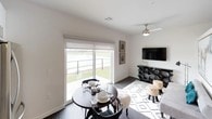 This single-floor residence showcases a clean, contemporary design throughout its well-appointed spaces. The kitchen is outfitted with a sleek combination of high-gloss white upper cabinetry and warm wood-toned lower cabinets, complemented by light quartz countertops, a subway tile backsplash, and a full suite of stainless steel appliances, including a range, microwave, and dishwasher. Dark hardwood-style flooring runs through the kitchen and main living areas, adding warmth and continuity.

The open living and dining area is bright and welcoming, anchored by a large sliding glass door that fills the space with natural light and provides direct views of an outdoor water feature. A ceiling fan overhead adds both function and style to the room.

The bedroom is a calm retreat finished with plush carpeting, a ceiling fan, and access to an adjoining space, with a walnut-toned door adding a refined touch. The closet features dual hanging rods and a wide shelf, offering practical and organized storage.

The bathroom carries the home's modern aesthetic with dark wood-plank flooring, a floating vanity with a white countertop, clean white walls, and a wood-grain door, creating a polished, spa-like atmosphere.