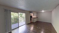 Located at 614 S 1st St in Austin's vibrant 78704 zip code, this single-floor unit offers a well-organized layout with consistent wood-style flooring throughout. The open living area is a standout feature, anchored by large sliding glass doors that lead to a private balcony overlooking lush, mature trees — filling the space with natural light and greenery. A textured popcorn ceiling runs throughout the main living areas, giving the space a classic residential character.

The kitchen is positioned adjacent to the living area and features a peninsula-style counter that provides separation while maintaining an open feel. White upper cabinetry, dark countertops, and black appliances — including an electric range with overhead ventilation and a full-size refrigerator — complete the functional cooking space.

The bedroom is a comfortable, well-proportioned room with a ceiling fan and light fixture, a window with blinds for natural light and privacy, and the same wood-style flooring found throughout. A hallway connects the bedroom to a full bathroom, which includes a tiled shower/tub combination with chrome fixtures. Additional doors off the hallway provide access to closet storage. The unit's neutral color palette and clean finishes make it a versatile and move-in-ready space.