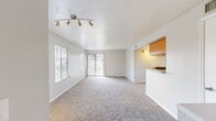 This single-floor residence is designed with a practical, open layout that maximizes usable space throughout. The living area is generously proportioned, featuring neutral-toned carpet, light gray walls, and a textured ceiling. A multi-directional track light fixture illuminates the room, while a large sliding glass door flanked by vertical blinds and an adjacent window with horizontal blinds allow for ample natural light. The living space connects seamlessly to the kitchen via a pass-through counter, lending an open, airy feel to the common areas.

The kitchen is efficiently arranged with warm wood-toned cabinetry, granite-style countertops, wood-look vinyl flooring, and stainless steel appliances including a refrigerator, stove, and built-in microwave. Louvered bi-fold doors provide additional storage access within the kitchen corridor.

The bedrooms are carpeted and finished in soft neutral tones, each offering a calm, versatile space. One bedroom features a ceiling fan with light fixture, while others include windows with blinds for natural light and privacy. The bathroom includes a full soaking tub with tile surround and a window for ventilation.