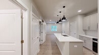 Located in Port Wentworth, Georgia, this single-story 2-bedroom, 2-bathroom home offers a well-designed layout with modern finishes throughout. The open-concept kitchen and living area serves as the heart of the home, featuring a large center island with a white quartz countertop and a built-in sink, complemented by stylish black pendant lighting overhead. The kitchen is equipped with stainless steel appliances—including a refrigerator, range, and microwave—alongside white shaker-style cabinetry and a classic subway tile backsplash. Wood-look plank flooring runs consistently through the entire home, creating a cohesive and easy-to-maintain aesthetic. The living area is bright and open, with access to the exterior through a glass-panel door and large windows with blinds that invite natural light. The primary bedroom is generously sized, featuring a ceiling fan, recessed lighting, and outdoor views through a wide window. It is supported by a spacious walk-in closet with wire shelving for ample storage. Both bathrooms are finished with neutral-toned cabinetry, white countertops, and tile-surround showers with glass doors. The second bedroom is well-proportioned and also benefits from a ceiling fan and natural light. The overall aesthetic is clean, neutral, and contemporary throughout.