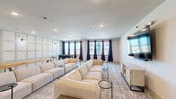 Located at 6490 Iron Horse Blvd in North Richland Hills, TX, this media room is a thoughtfully designed communal space built for entertainment and relaxation. The single-floor layout offers a generous, open feel, with recessed lighting throughout that provides consistent, comfortable illumination across the entire room.

The living area is anchored by multiple large, cream-colored modular sofas arranged to face a wall-mounted flat-screen television, which is paired with a light wood media console. Slim round side tables are positioned throughout for convenient use. The neutral-toned patterned carpet adds warmth and texture underfoot, complementing the clean white walls.

A standout design feature is the decorative wainscoting panel wall, which adds architectural character and visual depth to the space. Wall sconces accent this feature wall, further enhancing the room's polished aesthetic.

For recreation, the space includes a foosball table and a shuffleboard table, making it well-suited for social gatherings. A row of windows dressed with deep navy blue curtains lines one wall, allowing natural light to filter in while offering views of the surrounding community. The overall ambiance is modern, inviting, and versatile — equally suited for movie nights, casual socializing, or friendly competition.