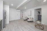 Located at 6559 Brynhurst Ave in Los Angeles, CA, this thoughtfully designed single-story unit offers a clean, contemporary living environment with a cohesive all-white palette and light wood-tone vinyl flooring throughout. The open-concept layout connects the kitchen and living areas seamlessly, creating a functional and airy atmosphere.

The kitchen is well-appointed with two-tone cabinetry — white uppers and gray lowers — paired with white countertops, a stainless steel refrigerator, electric range with overhead ventilation, dishwasher, and a dedicated wine rack. A stacked washer and dryer unit is conveniently located adjacent to the kitchen.

The living area accommodates a comfortable seating arrangement and is enhanced by recessed lighting and a wall-mounted mini-split HVAC system. A corridor lined with wall art leads to the private sleeping quarters.

The primary bedroom is generously proportioned, featuring multiple windows that allow ample natural light and a built-in closet. A second bedroom provides additional flexibility. Both bathrooms are finished in crisp white with matching vanities, tub-shower combinations, and light wood-tone flooring, maintaining the unit's consistent modern aesthetic throughout.