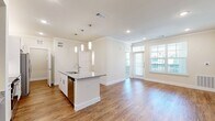 This thoughtfully designed 1-bedroom, 1-bathroom residence offers a functional and modern layout across a single floor. The open-concept kitchen and living area serves as the heart of the home, featuring warm hardwood-style flooring, crown molding, and recessed lighting. The kitchen is well-equipped with crisp white shaker cabinetry, granite countertops, a central island with a built-in sink, and a full suite of stainless steel appliances including a side-by-side refrigerator, electric range, and microwave. A dedicated built-in desk area adds a practical workspace to the kitchen. The living area is bathed in natural light from large windows and a glass-paneled entry door, creating a bright and welcoming atmosphere. The bedroom is a comfortable retreat with plush carpeting, a ceiling fan, and dual windows that invite natural light. It includes access to a generously sized walk-in closet outfitted with multiple shelving systems and hanging rods. The bathroom features hardwood-style flooring, a granite-topped vanity, and a full tub-shower combination with white subway tile surround. A hallway connects the rooms efficiently, completing this clean, modern, and highly functional layout.