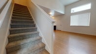 This two-story residence offers a thoughtfully designed layout across two well-defined levels. The main floor greets visitors with light hardwood-style flooring that extends throughout the open living and kitchen area. The kitchen is a functional centerpiece, outfitted with dark espresso cabinetry, light countertops, and a full suite of black appliances, including a refrigerator, range, microwave, and dishwasher. Ample upper and lower cabinet storage is complemented by a window above the sink, allowing natural light to brighten the workspace. The living area flows generously from the kitchen, benefiting from tall windows and elevated ceilings that enhance the sense of openness.

A carpeted staircase with a clean white half-wall leads to the upper level, where bedrooms are finished with plush neutral carpet and multiple windows fitted with blinds to control light. The upper level also features a bathroom with dark vanity cabinetry, a white countertop, and a large mirror. A convenient half bathroom is located on the main floor, maintaining the same consistent dark cabinetry and clean finishes found throughout the home. The overall aesthetic is clean, modern, and move-in ready.