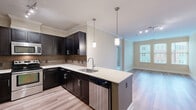 Located at 12190 Waveland St in Fairfax, VA, this thoughtfully designed 2-bedroom, 2-bathroom residence offers a comfortable and functional single-floor layout. The open-concept kitchen and living area serves as the heart of the home, showcasing rich dark cabinetry with sleek hardware, light granite countertops, a tile backsplash, and stainless steel appliances. A peninsula with pendant lighting provides additional prep space and doubles as a casual dining area. Light hardwood-style flooring extends throughout the main living spaces, complemented by crown molding that adds a refined touch. The living room benefits from natural light through a large window with exterior views of the surrounding neighborhood. Both bedrooms feature plush carpeting, neutral warm-toned walls, and windows that invite natural light. The primary bathroom is well-appointed with a dual-sink vanity, dark cabinetry, granite countertops, a large mirror, and a tub-shower combination with tiled surround. The second bathroom mirrors the same quality finishes. A walk-in closet with wire shelving systems provides generous storage. Additional highlights include built-in shelving in the living area, an in-unit washer and dryer, and two dedicated closet spaces for practical everyday living.