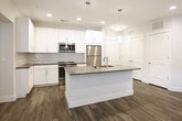 Located at 5775 Glenridge Dr NE in Sandy Springs, GA, this single-floor residence offers a clean, contemporary design with thoughtful finishes throughout. The open-concept kitchen serves as the heart of the space, showcasing white shaker cabinetry, a subway tile backsplash, dark quartz countertops, and a full suite of stainless steel appliances including a refrigerator, range, and microwave. A generously sized kitchen island with a built-in sink and pendant lighting above provides both additional prep space and a natural gathering point. Wood-look luxury vinyl plank flooring runs throughout the main living and kitchen areas, lending a warm yet modern aesthetic. The entry corridor is well-organized, with multiple doors offering convenient access to storage and adjacent rooms. The bedroom features soft carpeting, a ceiling fan with light fixture, and a window with blinds that allows natural light to fill the room. The bathroom is finished with white cabinetry, gray quartz countertops, a framed mirror, and matching wood-look flooring that ties the space together cohesively. Recessed lighting and flush-mount ceiling fixtures illuminate the space evenly throughout. The overall design palette of whites, grays, and warm wood tones creates a bright, neutral, and inviting atmosphere well-suited for comfortable everyday living.