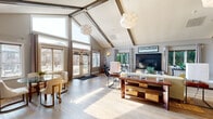 Located at 8500 Tree Top Ct S in Miamisburg, Ohio, this single-floor space makes a striking first impression with its dramatic vaulted ceilings accented by exposed wood beams and elegant globe pendant lighting. Light hardwood flooring flows seamlessly throughout, unifying the open-concept layout and enhancing the bright, airy ambiance.

The expansive living area is anchored by a sleek, dark-paneled fireplace flanked by large windows that invite abundant natural light and views of the surrounding greenery. Generous ceiling height and thoughtfully placed wall sconces create a warm yet spacious atmosphere. French doors with transom windows at the entry further amplify the sense of openness, connecting the interior to the outdoors.

A dedicated dining area near the entry accommodates a round glass-top table with comfortable seating, bathed in natural light from the nearby windows. The kitchen features dark cabinetry, stainless steel appliances, and a granite-topped peninsula with stylish bar stools — ideal for casual dining and entertaining. Track lighting overhead adds functional illumination to the cooking space.

Together, these areas form a cohesive, well-designed environment that balances architectural character with comfortable, modern living in the heart of Miamisburg.
