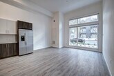 Located at 730 16th Street in Sacramento, CA, this studio unit at The Mansion offers a well-designed, single-floor open layout that maximizes functionality and style. Light wood-tone vinyl flooring runs throughout the entire space, providing a clean, cohesive aesthetic.

The living area benefits from a striking floor-to-ceiling window with transom, flooding the room with natural light and offering views of the tree-lined street outside. The soaring ceiling height enhances the sense of openness throughout.

The kitchen is thoughtfully appointed with a two-tone cabinet design — warm wood lower cabinets paired with crisp white upper cabinets — complemented by a white subway tile backsplash and light quartz countertops. A full suite of stainless steel appliances includes a refrigerator, electric range, over-the-range microwave, and dishwasher, along with a single-basin sink with a modern pull-down faucet.

The bathroom features light wood-tone flooring consistent with the rest of the unit, a wood-toned vanity with a white countertop, and a full tub-shower combination with elegant marble-style wall surround and a curved shower rod. The bright white walls throughout the unit contribute to a fresh, contemporary ambiance ideal for urban living.