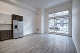 Located at 730 16th Street in Sacramento, CA, this studio unit at The Mansion offers a well-designed, single-floor open layout that maximizes functionality and style. Light wood-tone vinyl flooring runs throughout the entire space, providing a clean, cohesive aesthetic.

The living area benefits from a striking floor-to-ceiling window with transom, flooding the room with natural light and offering views of the tree-lined street outside. The soaring ceiling height enhances the sense of openness throughout.

The kitchen is thoughtfully appointed with a two-tone cabinet design — warm wood lower cabinets paired with crisp white upper cabinets — complemented by a white subway tile backsplash and light quartz countertops. A full suite of stainless steel appliances includes a refrigerator, electric range, over-the-range microwave, and dishwasher, along with a single-basin sink with a modern pull-down faucet.

The bathroom features light wood-tone flooring consistent with the rest of the unit, a wood-toned vanity with a white countertop, and a full tub-shower combination with elegant marble-style wall surround and a curved shower rod. The bright white walls throughout the unit contribute to a fresh, contemporary ambiance ideal for urban living.