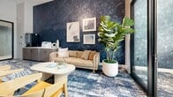 Located at 27930 Cabot Rd in Laguna Niguel, CA, this thoughtfully designed professional suite offers a cohesive blend of modern aesthetics and functional workspaces across a single floor. The central lounge area serves as the heart of the suite, featuring soaring ceilings, a striking pendant light fixture, and bold blue abstract-patterned carpeting that flows throughout the space. A comfortable neutral sofa, a round marble-top coffee table, and sculptural yellow accent chairs create a welcoming and collaborative atmosphere.

Dramatic dark marble-effect accent walls punctuate key areas, adding depth and sophistication to the overall design. Lush fiddle-leaf fig trees and curated artwork contribute warmth and a refined, coastal-inspired character. Black-framed glass partitions and doors divide the space into distinct zones while maintaining an open, light-filled feel and providing views through to the exterior.

Several private offices branch off from the central lounge, each enclosed by floor-to-ceiling glass walls that allow natural light to filter freely. A dedicated conference room accommodates a full-sized meeting table with ample seating, and features an ocean-themed mural wall alongside framed coastal photography. Throughout the suite, high ceilings, recessed lighting, and glass-fronted rooms combine to create a professional yet inviting environment well-suited for modern business needs.