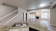 Located at 2803 Riverside Pkwy in Grand Prairie, Texas, this two-story residence offers a thoughtfully designed layout that balances functionality and comfort. The main living area greets visitors with wood-style flooring, neutral-toned walls, and elegant arched architectural details that lend a refined character to the space. A ceiling fan and natural light from large windows, including French doors, enhance the inviting atmosphere of the living room, which is anchored by a classic fireplace.

The kitchen is well-appointed with white cabinetry, granite countertops, a double stainless steel sink set into a peninsula, and a suite of stainless steel appliances including a refrigerator, electric range, and over-the-range microwave. The open-concept design allows seamless flow between the kitchen and living areas.

A carpeted staircase with white-painted balusters connects the two floors, adding a traditional aesthetic touch. Upstairs, the space continues with wood-style flooring and includes a generously sized walk-in closet outfitted with wire shelving for ample storage. A bathroom with tile flooring completes the upper level. Throughout, the consistent use of neutral tones and clean finishes creates a cohesive and welcoming environment.