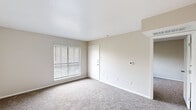 Located at 9821 Summerwood Cir in Dallas, Texas, this two-bedroom, one-bathroom residence offers a practical and well-organized single-floor layout. The living area features neutral-toned carpet, smooth walls with clean white trim, and a large window fitted with horizontal blinds that allows natural light to fill the space. A pass-through opening connects the living area to the kitchen, enhancing the sense of openness between rooms. The kitchen is outfitted with white shaker-style cabinetry, light wood-tone flooring, white countertops, and stainless steel appliances including a full-size refrigerator and range. The primary bedroom is generously proportioned relative to the overall footprint, featuring carpeted floors, a closet, and a bright window with outdoor views of surrounding greenery. The second bedroom also includes carpeted flooring and a large window that brings in natural light. The bathroom is clean and functional, equipped with a tiled shower-tub combination, a toilet, and a vanity with white cabinetry. Neutral, warm tones are used consistently throughout the residence, contributing to a cohesive and move-in-ready ambiance. The efficient layout makes practical use of every square foot of available space.