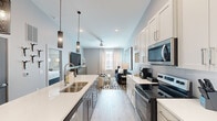 This thoughtfully designed one-bedroom, one-bathroom residence offers a contemporary open-concept layout that maximizes every square foot. The kitchen serves as a central focal point, featuring white shaker cabinetry, quartz countertops, stainless steel appliances, and a large island with seating — all illuminated by striking pendant lighting that adds a designer touch. The seamless flow from kitchen to living area creates an inviting, functional space ideal for both everyday living and entertaining.

The living room is bright and well-proportioned, benefiting from natural light through large windows dressed with elegant floor-to-ceiling curtains. Light wood-tone flooring runs throughout, tying the space together cohesively. A ceiling fan adds both style and practicality.

The bedroom is a well-sized retreat featuring a dramatic four-poster canopy bed frame in brushed gold, bold drapery, and a wall-mounted TV, offering both comfort and visual sophistication. A dedicated closet provides practical storage.

The bathroom is cleanly finished with white cabinetry, quartz vanity surfaces, wood-look tile flooring, and a glass-enclosed walk-in shower with white tile surround. Every room reflects a consistent modern aesthetic with upscale detailing throughout.