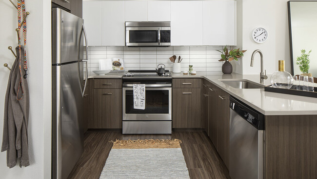 Cocina del apartamento con electrodomésticos de acero inoxidable, encimeras de cuarzo y pisos estilo madera. - Griffis Cherry Creek