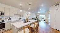 Located in Draper, Utah, this well-designed 2-bedroom, 1-bathroom residence offers a thoughtful open-concept layout that seamlessly connects the kitchen, dining, and living areas. The kitchen is a standout feature, showcasing sleek gray cabinetry, white quartz countertops, stainless steel appliances, and a central island with pendant lighting and bar seating — ideal for both meal preparation and casual dining. Warm wood-tone flooring flows throughout the main living areas, enhancing the bright, airy ambiance created by recessed lighting throughout.

The living room is generously proportioned, featuring sliding glass doors that open onto a private balcony, allowing abundant natural light and outdoor views to pour in. Both bedrooms are carpeted and well-sized, with the primary bedroom offering a large window for additional natural light. The second bedroom provides a comfortable and functional space. A full bathroom features a clean, modern design with a single-sink vanity, white cabinetry, and a tub-shower combination. Two dedicated closets offer practical storage throughout the home. The overall aesthetic is contemporary and inviting, with a neutral palette that creates a calm, cohesive living environment.