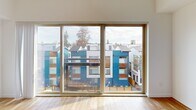 Located on the fourth floor at 8022 15th Ave NW in Seattle's Crown Hill/Ballard neighborhood, Unit 406 is a thoughtfully designed studio that maximizes its efficient footprint. The unit features warm hardwood flooring throughout the main living area, complemented by clean white walls that enhance the sense of openness and light.

The combined kitchen and living room forms the heart of the unit. The kitchen is outfitted with a full suite of stainless steel appliances — including a refrigerator, electric range, built-in microwave, and dishwasher — set against contemporary two-tone cabinetry with dark lower cabinets and warm wood-toned uppers, all finished with light countertops. A hallway entry leads past a glass-panel sliding closet and an in-unit stacked washer/dryer, keeping everyday essentials neatly organized. Large sliding glass windows in the living area flood the space with natural light and frame views of the surrounding Seattle streetscape and neighboring architecture.

The bathroom is finished with warm-toned flooring, a wood-grain vanity with a white countertop, and clean white walls, maintaining the unit's consistent modern aesthetic throughout. The overall design is contemporary and functional, making efficient use of every square foot.