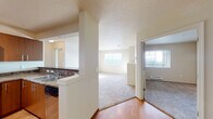 This single-floor residence offers a thoughtfully designed layout with a seamless flow between living spaces. The kitchen is a standout feature, equipped with stainless steel appliances including a refrigerator, range, and microwave, complemented by rich warm-toned cabinetry, granite-style countertops, and hardwood flooring. Track lighting overhead enhances both functionality and ambiance. A pass-through counter connects the kitchen to the adjacent living area, which transitions to plush carpeting underfoot.

The living and dining areas are open and airy, benefiting from multiple windows that invite natural light and offer outdoor views. A separate bedroom features neutral carpet, a baseboard heater, and a window framing elevated views of the surrounding area, creating a calm and comfortable retreat.

The bathroom is well-appointed with a wide vanity topped with granite-style counters, warm wood cabinetry with ample drawer storage, hardwood flooring, and a large illuminated mirror. A dedicated in-unit laundry area houses a full-sized washer and dryer with overhead wire shelving, adding everyday convenience. Throughout the space, a neutral color palette and textured ceilings contribute to a clean, cohesive aesthetic.