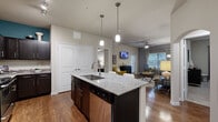 This single-floor, 3-bedroom, 2-bathroom residence offers a thoughtfully designed open-concept layout that maximizes functionality and flow. The kitchen serves as the centerpiece of the living area, anchored by a large island with granite countertops, an undermount sink, and dark espresso cabinetry. Stainless steel appliances, a mosaic tile backsplash, and stylish pendant lighting complete the space. The kitchen opens seamlessly into the living and dining area, which features wood-style flooring, a ceiling fan, and ample natural light from large windows with window treatments. A connecting hallway with an arched passage links the living area to the private quarters. The primary bedroom offers plush carpeting, a ceiling fan, generous natural light, and access to a walk-in closet with wire shelving. The two bathrooms include granite-topped vanities with dark cabinetry, and a tiled tub-shower combination. Additional features include a second walk-in closet and a carpeted hallway connecting the bedrooms. Throughout the residence, a neutral color palette with warm accent walls creates a cohesive and inviting ambiance.
