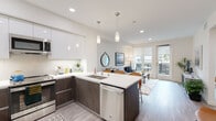 This single-story unit in Alameda, California, showcases a thoughtfully designed open-concept floor plan with clean, contemporary finishes throughout. Light wood-style flooring runs continuously through the living areas, enhancing the sense of cohesion and space.

The kitchen is a standout feature, equipped with stainless steel appliances including a refrigerator, range, built-in microwave, and dishwasher. Cabinetry combines dark wood lower cabinets with high-gloss white upper cabinets, complemented by white quartz countertops and a subway tile backsplash. A peninsula with seating for multiple bar-height chairs doubles as a dining area and casual workspace. Pendant lighting above the peninsula adds a polished touch.

The living area is bright and welcoming, with recessed lighting and direct access to a private outdoor balcony through glass-paneled doors, allowing natural light to flow freely into the space.

The bedroom is generously sized, featuring large windows with views of the surrounding neighborhood and ample room for substantial furniture. The full bathroom includes a combination tub and shower with tile surround, a dark wood vanity with a white countertop, and a large mirror.