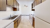 Located at 1502 21st Ave S in Fargo, North Dakota, this one-bedroom, one-bathroom unit offers a practical and comfortable layout across a single floor. The galley-style kitchen is lined with warm wood cabinetry on both sides, providing ample storage space. White appliances including a coil-top range, oven, and refrigerator are complemented by light tile flooring and a double-basin sink. A ceiling fan overhead adds airflow to the kitchen and adjoining living area. The living room is carpeted and features a sliding glass door that opens to a private balcony, allowing natural light to fill the space and offering views of surrounding trees and the neighborhood. A wall-mounted AC unit and baseboard heating ensure year-round climate control. The spacious primary bedroom is also carpeted, featuring a large window that brings in additional natural light, a built-in closet with bifold doors, and continued baseboard heating. The bathroom is clean and functional, featuring a tub and shower combination enclosed by a frosted glass sliding door with chrome framing. Neutral wall tones and dark baseboards throughout create a cohesive, understated aesthetic.