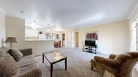 This single-floor, 1-bedroom, 1-bathroom residence offers a thoughtfully organized layout that maximizes comfort and functionality. The open-concept living room is carpeted and bathed in natural light from a set of French doors that lead to an outdoor area, framed by crown molding that adds a refined architectural touch. The space flows seamlessly into the combined dining room and kitchen, where a pass-through window connects the two areas. The kitchen features white cabinetry, white appliances including a refrigerator, electric range, built-in microwave, and dishwasher, all set over clean tile flooring. The dining area accommodates a round table and is lit by a classic chandelier. A concealed laundry closet off the dining area houses a full-size washer and dryer. The bedroom is a comfortable retreat with plush carpeting, crown molding, and direct access to a spacious walk-in closet with built-in shelving. The full bathroom includes a tiled shower-tub combination, a white vanity, and tile flooring. Throughout the residence, warm neutral tones and crown molding create a cohesive and inviting ambiance.
