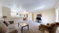 This single-floor, 1-bedroom, 1-bathroom residence offers a thoughtfully organized layout that maximizes comfort and functionality. The open-concept living room is carpeted and bathed in natural light from a set of French doors that lead to an outdoor area, framed by crown molding that adds a refined architectural touch. The space flows seamlessly into the combined dining room and kitchen, where a pass-through window connects the two areas. The kitchen features white cabinetry, white appliances including a refrigerator, electric range, built-in microwave, and dishwasher, all set over clean tile flooring. The dining area accommodates a round table and is lit by a classic chandelier. A concealed laundry closet off the dining area houses a full-size washer and dryer. The bedroom is a comfortable retreat with plush carpeting, crown molding, and direct access to a spacious walk-in closet with built-in shelving. The full bathroom includes a tiled shower-tub combination, a white vanity, and tile flooring. Throughout the residence, warm neutral tones and crown molding create a cohesive and inviting ambiance.