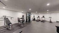 Located at 6450 Bayers Road in Halifax, NS, this fitness center offers a thoughtfully designed exercise space across a single floor. The room is finished with crisp white walls, recessed lighting, and durable speckled rubber flooring that provides both safety and comfort during workouts.

The space is well-equipped to support a wide range of fitness routines. Cardio equipment includes multiple treadmills, an elliptical trainer, and a Matrix spin bike, all arranged to allow ample room for use. Strength training is supported by a multi-station cable machine, a leg press/extension machine, and a dedicated free weights area featuring a tiered dumbbell rack and adjustable benches. Stability balls and kettlebells round out the functional training options.

Large wall-mounted mirrors span key sections of the room, visually expanding the space and allowing users to monitor their form during exercise. A water fountain is conveniently located within the facility, along with a sanitation station to support cleanliness. The open layout maximizes the available floor area, ensuring a comfortable and uncluttered environment. The overall ambiance is clean, modern, and functional — well-suited to residents looking for a convenient and fully equipped place to maintain an active lifestyle.